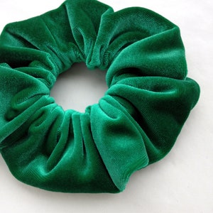 Pu&ograve; includere: Primo piano di un elastico per capelli in velluto verde. Il tessuto &egrave; arricciato, creando un aspetto strutturato e voluminoso. L'elastico per capelli &egrave; di un ricco colore verde smeraldo. Accessorio per capelli.