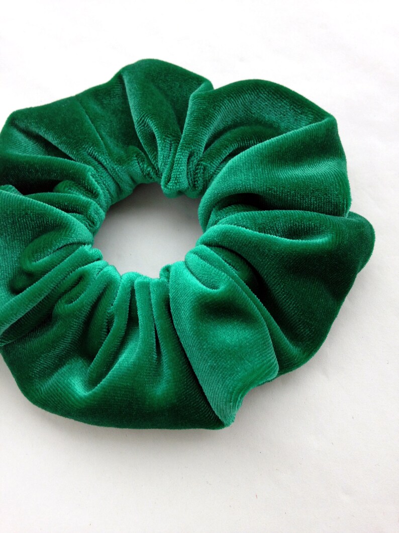 Pu&ograve; includere: Primo piano di un elastico per capelli in velluto verde. Il tessuto &egrave; arricciato, creando un aspetto strutturato e voluminoso. L'elastico per capelli &egrave; di un ricco colore verde smeraldo. Accessorio per capelli.