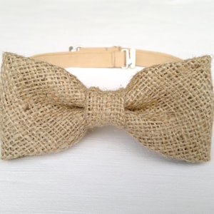 May include: A tan burlap bow tie with a matching adjustable neckband and silver-colored metal hardware. The bow tie is made of a woven, textured fabric. This accessory is suitable for weddings, parties, or everyday wear.