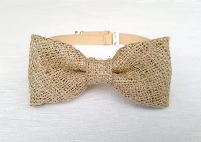 May include: A tan burlap bow tie with a matching adjustable neckband and silver-colored metal hardware. The bow tie is made of a woven, textured fabric. This accessory is suitable for weddings, parties, or everyday wear.