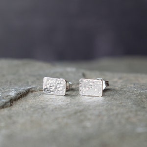 May include: A pair of silver rectangle stud earrings with a hammered texture.