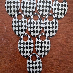 May include: A collection of ten oval-shaped pendants with a black and white checkered pattern. Each pendant has a small circular hole at the top. The pendants are arranged on a brown wooden surface.