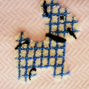 May include: A handmade, textured dog-shaped applique in blue and cream, with a black collar and details. The applique is set against a pink herringbone pattern background, creating a charming, whimsical design.