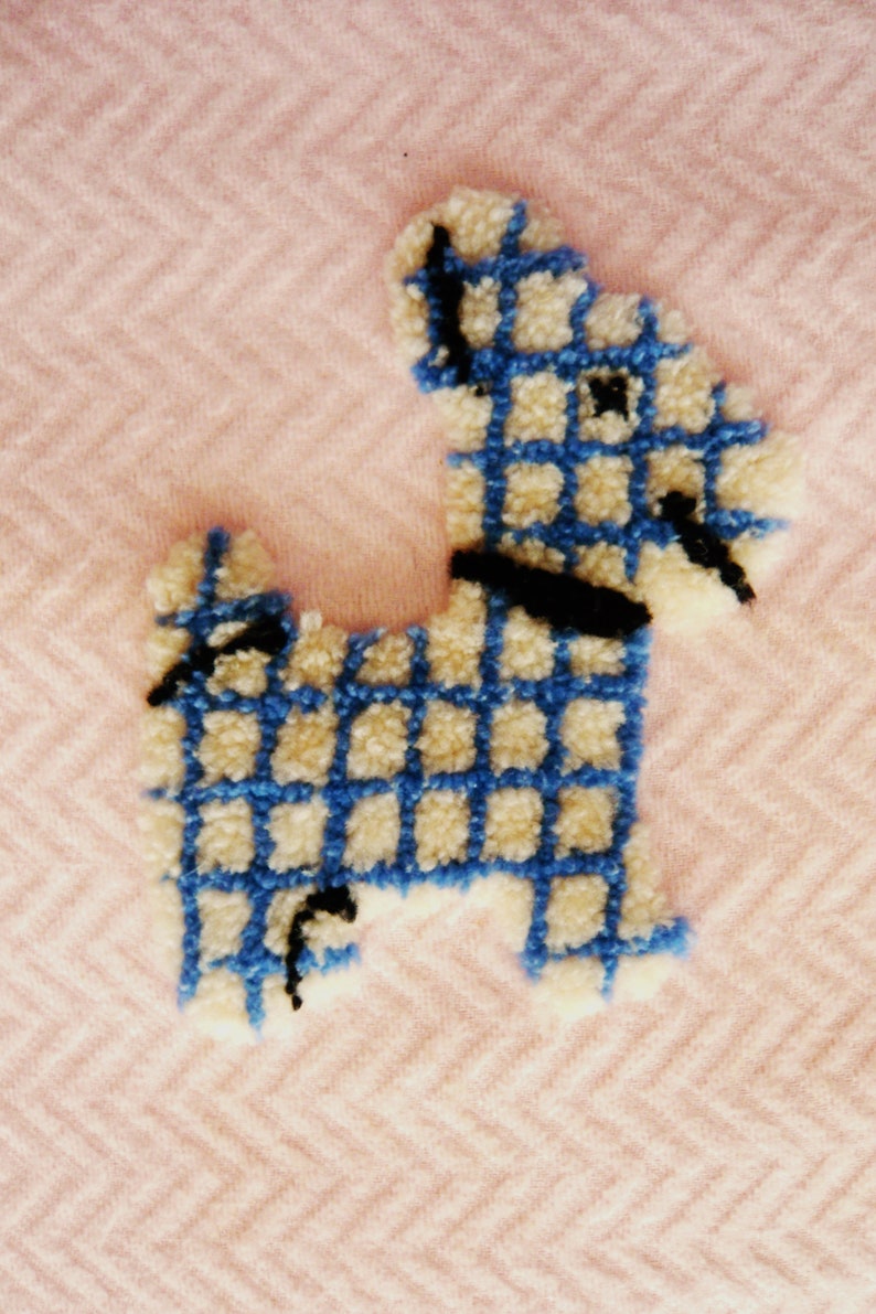 May include: A handmade, textured dog-shaped applique in blue and cream, with a black collar and details. The applique is set against a pink herringbone pattern background, creating a charming, whimsical design.