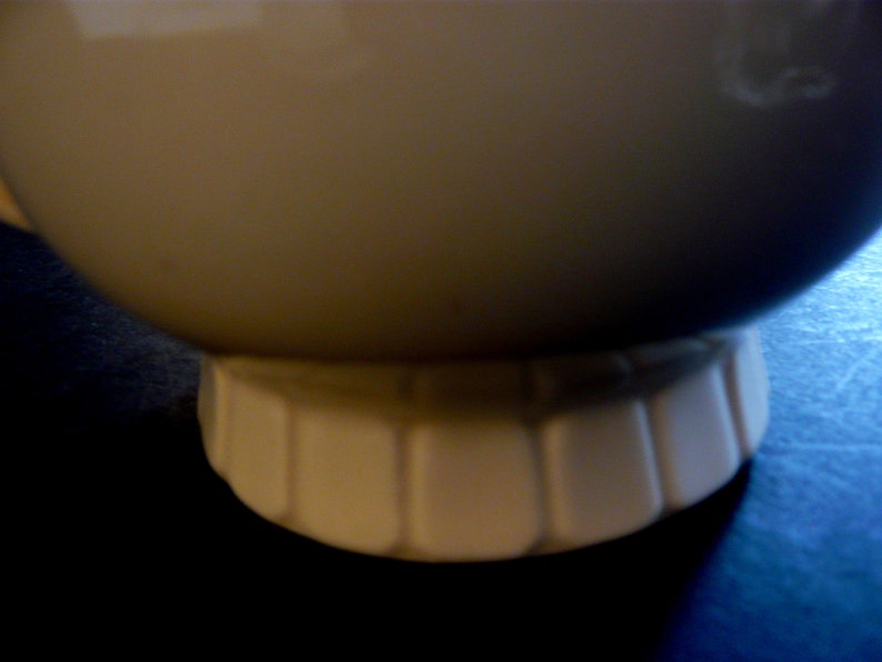 May include: A cream-colored ceramic bowl with a rounded body and a fluted base. The bowl's surface is smooth and glossy, and the base has a series of vertical indentations. The bowl is likely for serving food.