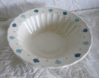 May include: A white ceramic bowl with a fluted design and a blue and green floral pattern around the rim.