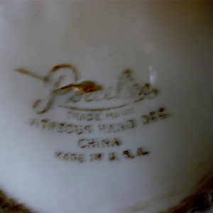 May include: Close-up of a white ceramic surface with brown text. The text includes the word "Porcelia" in a cursive font, along with "TRADE MARK", "VITREOUS HAND DEC", "CHINA", and "MADE IN U.S.A."