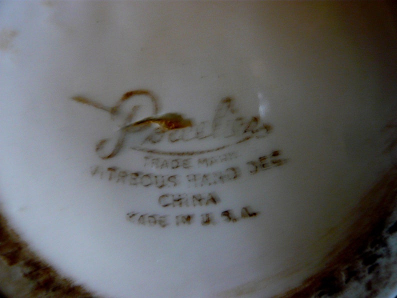 May include: Close-up of a white ceramic surface with brown text. The text includes the word "Porcelia" in a cursive font, along with "TRADE MARK", "VITREOUS HAND DEC", "CHINA", and "MADE IN U.S.A."