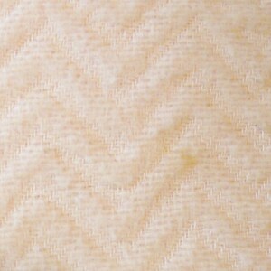 May include: Close-up of a textured fabric with a diagonal herringbone pattern. The fabric has a light beige color with subtle variations in tone, creating a soft, inviting appearance. The weave is tight and detailed.