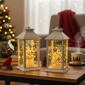 May include: Two white distressed wooden lanterns with glass panels, each containing a pillar candle and warm fairy lights. One lantern features the text "Cardinals appear when Angels are near" and a red cardinal illustration on the glass.