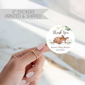 May include: Round thank you sticker with a watercolor illustration of a sleeping fawn with green leaves and white flowers. The text "Thank You" is in brown lettering. The text "Karen's Baby Shower 4.22.2022" is in brown lettering.