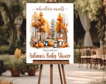 May include: A wooden easel displays a sign with the text "adventure awaits" and "Welcome to Autumn's Baby Shower." The sign features a watercolor illustration of woodland animals, pumpkins, and autumn trees. The background shows an outdoor event setting.