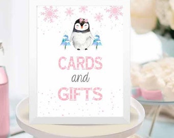 May include: A white sign with a pink border and a penguin illustration. The sign says "Cards and Gifts" in pink letters with a white snowflake background.