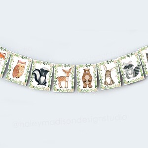 May include: A woodland animal banner with a fox, owl, skunk, deer, bear, rabbit, raccoon, and squirrel. Each animal is surrounded by green leaves and pink flowers.