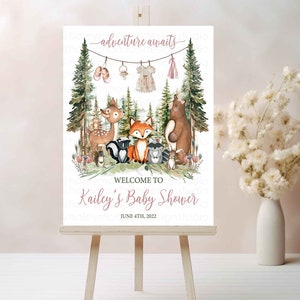 K&ouml;nnte beinhalten: Ein wei&szlig;es Schild mit Waldmotiv f&uuml;r eine Babyparty. Das Schild zeigt ein Reh, einen Fuchs, einen B&auml;ren, einen Waschb&auml;ren und andere Waldtiere. Der Text auf dem Schild lautet "adventure awaits" und "Welcome to Kailey's Baby Shower June 4th, 2022".