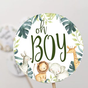 May include: A round, white cupcake topper with green foliage and animal illustrations. The topper features the text "oh boy" in green lettering. The animals include a zebra, lion, elephant, and giraffe.