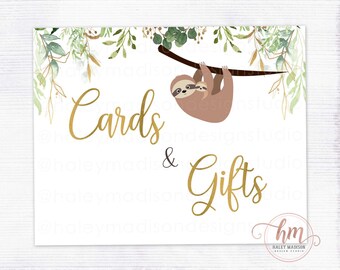 May include: A white sign with gold text that reads "Cards & Gifts". A watercolor illustration of a sloth with a baby sloth hanging on its back is above the text. The sign is decorated with green and gold watercolor leaves.