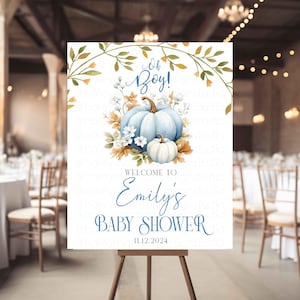Pode incluir: Uma placa de chá de bebé num cavalete. A placa apresenta um design em aquarela com abóboras azuis, flores e o texto "Oh Boy!" e "Welcome to Emily's Baby Shower 11.12.2024". A placa está montada num espaço de eventos decorado.