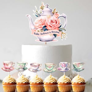 May include: A cake decorated with a floral teapot cake topper and six cupcake toppers. The teapot topper has pink roses and the text "Baby Anderson is Brewing". The cupcake toppers feature teacups with floral designs.