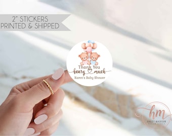 May include: A circular 2-inch sticker featuring two brown teddy bears holding a cluster of pink and blue balloons. The text reads Thank You beary much and Karen's Baby Shower in brown script and print fonts, centered on a white background.