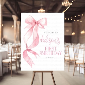 May include: A white sign with a pink watercolor bow and the text "Welcome to Addison's First Birthday 7.20.2020".