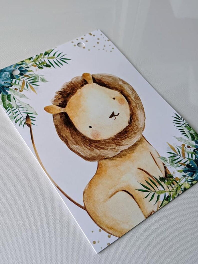 Puede incluir: Una ilustraci&oacute;n de acuarela de un le&oacute;n con una melena marr&oacute;n y un cuerpo marr&oacute;n claro. El le&oacute;n est&aacute; rodeado de hojas verdes y purpurina dorada.