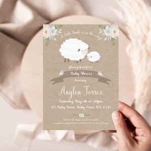 Puede incluir: Una invitación de baby shower marrón y blanca con un cordero blanco y un cordero más pequeño. La invitación dice "¡Un pequeño cordero está en camino!" y "Por favor, únase a nosotros para una Baby Shower en honor a Anglea Torres".