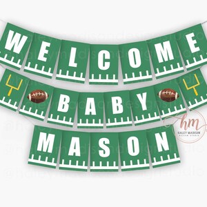 May include: A green banner with white text that reads "WELCOME BABY MASON." The banner has a football theme, with footballs and goalposts. The banner is strung on a white string.