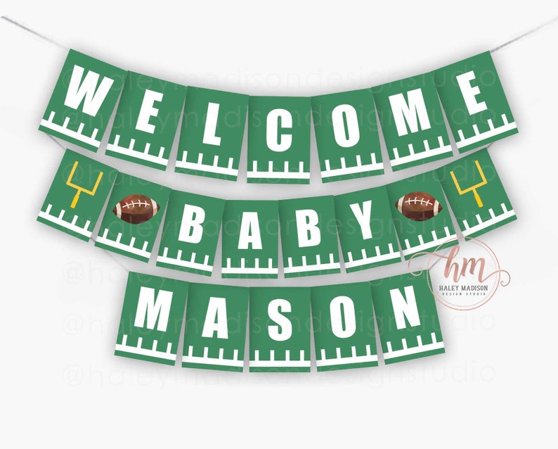 May include: A green banner with white text that reads "WELCOME BABY MASON." The banner has a football theme, with footballs and goalposts. The banner is strung on a white string.