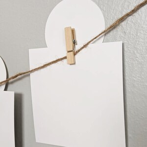 May include: A white card is clipped to a string with a wooden clothespin. The string is attached to a white circle.