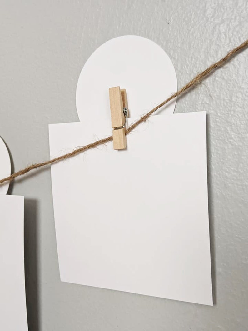 May include: A white card is clipped to a string with a wooden clothespin. The string is attached to a white circle.