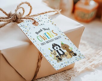 May include: A rectangular white gift tag with a brown twine string featuring a pattern of blue and brown paw prints. The text reads Thank You! OWEN'S FIRST BIRTHDAY PAWTY! with an illustration of several dogs wearing party hats.