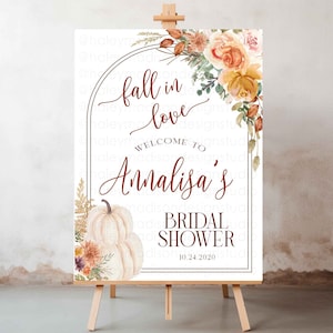 Puede incluir: Un letrero de bienvenida para una despedida de soltera sobre un caballete. El letrero presenta el texto "Fall in Love" y "Welcome to Annalisa's Bridal Shower" en una escritura decorativa. El letrero está decorado con ilustraciones florales y de calabazas.