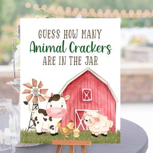 May include: A red barn with a white window and a white door. A cow with black and white spots stands in front of the barn. A white lamb stands next to the cow. Two yellow chicks are in front of the cow and lamb. A sign says "Guess how many Animal Crackers are in the jar."