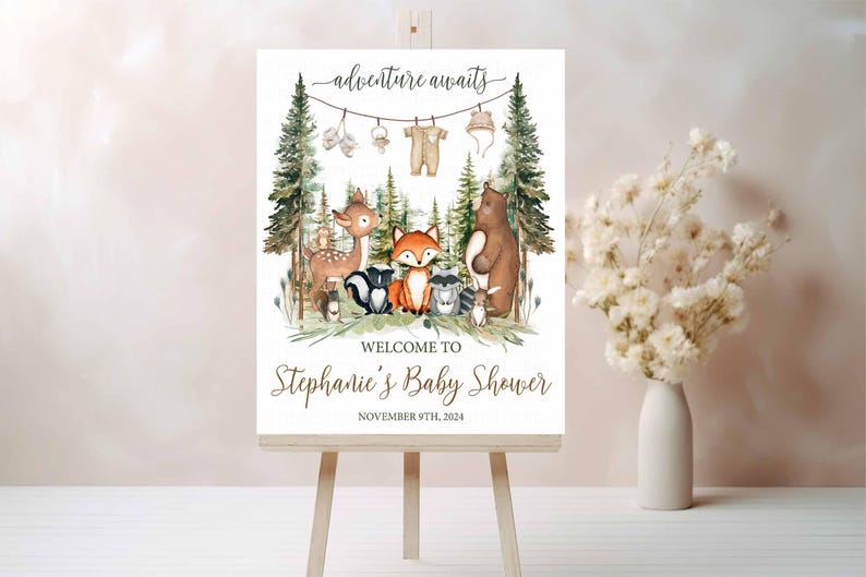 K&ouml;nnte beinhalten: Ein wei&szlig;es Willkommens-Schild mit Waldmotiv. Das Schild zeigt ein Reh, einen Fuchs, einen Waschb&auml;r, einen B&auml;ren und einen Baby-Strampler, der an einer W&auml;scheleine h&auml;ngt. Der Text auf dem Schild lautet "adventure awaits" und "Welcome to Stephanie's Baby Shower, November 9th, 2024".