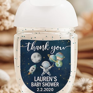 May include: Clear hand sanitizer bottle with a white cap. The label features a navy blue background with a rocket ship, astronaut, planets, and the words "thank you" and "Lauren's Baby Shower 2.2.2020" in white script.