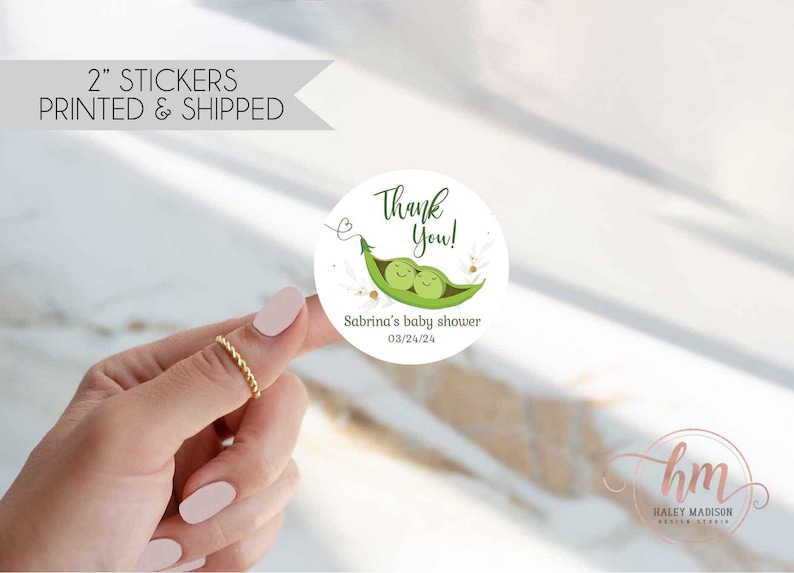 May include: A round 2-inch sticker featuring a green pea pod illustration with two smiling peas inside. The text reads Thank You!, Sabrina's baby shower, and 03/24/24. The design includes small floral accents and a thin heart-shaped vine.