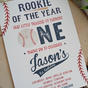 K&ouml;nnte beinhalten: Eine Baseball-Motto-Einladung zum ersten Geburtstag mit rotem und blauem Text. Die Einladung lautet "Rookie of the Year" und "Our little slugger is turning one." Sie enth&auml;lt auch den Namen "Jason's" sowie Datum und Uhrzeit der Party.