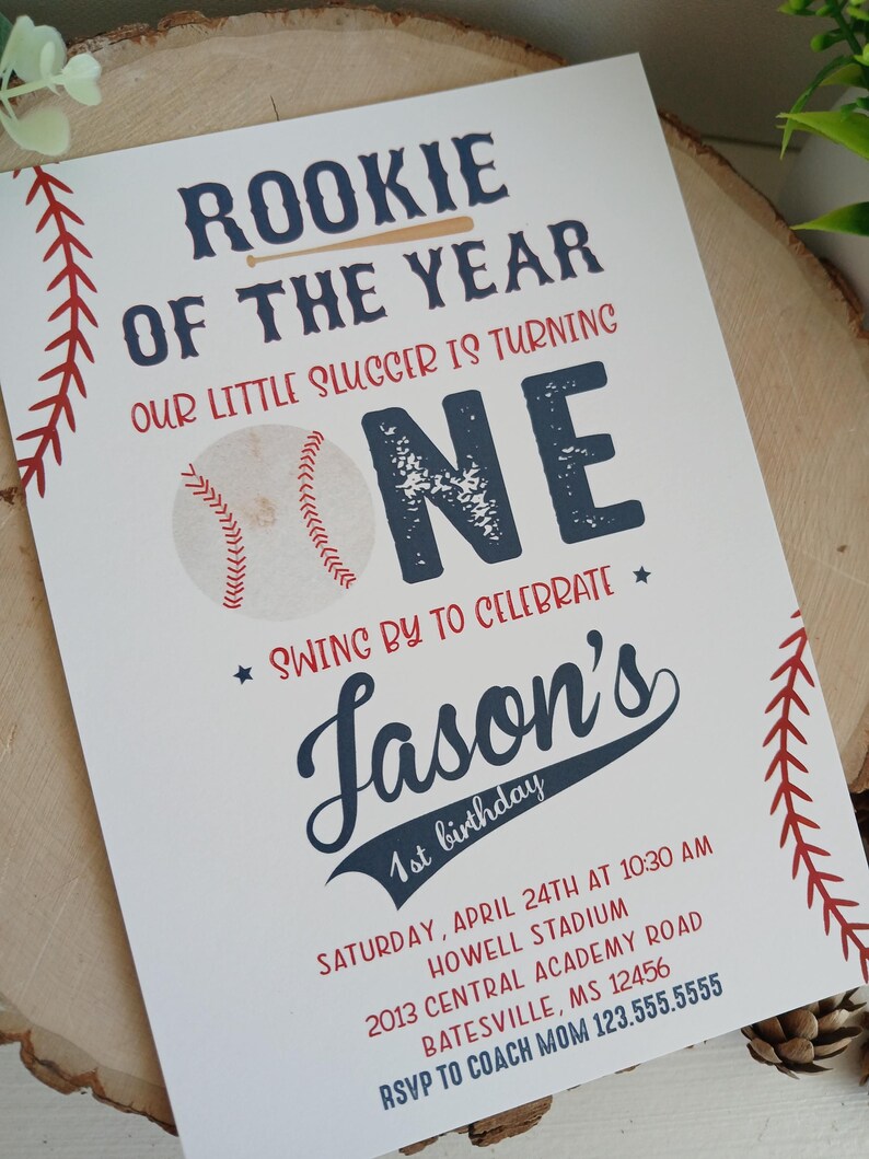 K&ouml;nnte beinhalten: Eine Baseball-Motto-Einladung zum ersten Geburtstag mit rotem und blauem Text. Die Einladung lautet "Rookie of the Year" und "Our little slugger is turning one." Sie enth&auml;lt auch den Namen "Jason's" sowie Datum und Uhrzeit der Party.