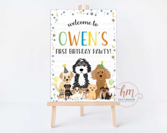 May include: A party sign on a wooden easel with the text "welcome to OWEN'S FIRST BIRTHDAY PAWTY!" in colorful letters. The sign features illustrations of various dog breeds, paw prints, and confetti.