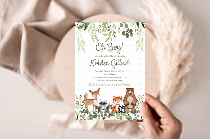 May include: A baby shower invitation with a woodland theme. The invitation features a green leafy border with a brown bear, a deer, a fox, a raccoon, and an owl. The text on the invitation reads "Oh Boy!" and "Kristen Gilbert".