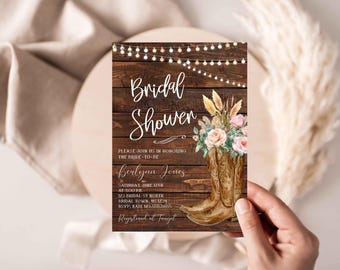 Pode incluir: Um convite rústico para um chá de panela com um fundo de madeira e um par de botas de cowboy marrons decoradas com flores rosa e brancas. O texto diz "Bridal Shower" e "Por favor, junte-se a nós para homenagear a noiva Berlyna Jones".