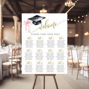 Può includere: Un tableau segnaposto a tema laurea su cavalletto. Il cartello presenta un cappello di laurea nero con un fiocco rosa e la scritta dorata "welcome" e "PLEASE FIND YOUR SEAT". Il grafico elenca i nomi sotto i numeri dei tavoli da 1 a 12.