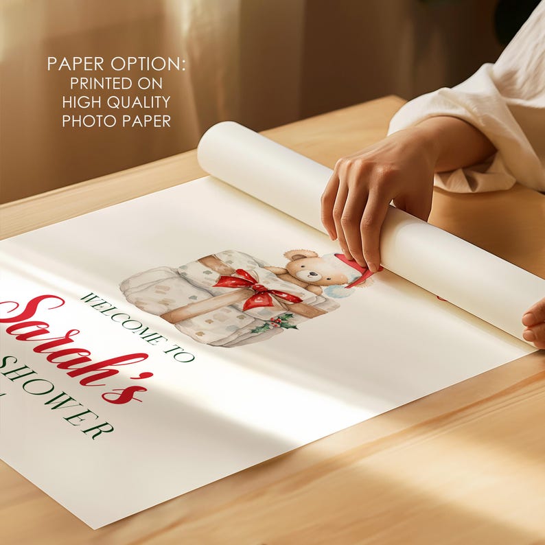 May include: A white poster printed on high quality photo paper featuring the text "WELCOME TO Sarah's SHOWER" in red and black lettering. The design includes a watercolor illustration of a teddy bear wearing a red hat sitting on gift boxes.