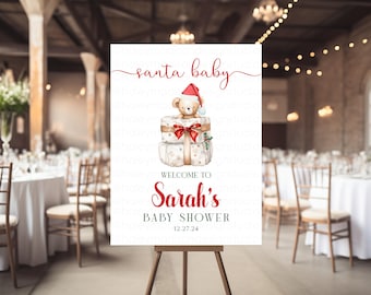 May include: A white rectangular sign featuring the red text santa baby at the top, a watercolor illustration of a teddy bear wearing a red Santa hat sitting on two wrapped gifts, and the text WELCOME TO Sarah's BABY SHOWER 12.27.24 below.