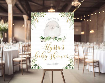 May include: A white welcome sign with green foliage and a white lamb illustration. The sign reads "Welcome to Alyssa's Baby Shower, February 26, 2022".