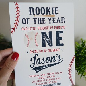 K&ouml;nnte beinhalten: Eine Baseball-Motto-Einladung zum ersten Geburtstag mit roten und blauen Akzenten. Die Einladung zeigt eine Baseball-Grafik und den Text "Rookie of the Year" und "Our little slugger is turning one". Die Einladung enth&auml;lt auch den Namen "Jason's" sowie Datum und Uhrzeit der Party.
