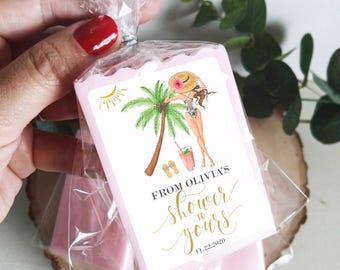 May include: A pink soap bar with a white label featuring a cartoon woman in a swimsuit and a straw hat, palm trees, and the text "From Olivia's Shower to Yours 11.22.2020".