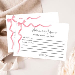 May include: A white card with pink ribbon designs and the text "Advice & Wishes for The Almost Mrs. Gelles". The card has lines for writing advice and wishes.