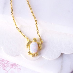 May include: A gold chain necklace with a small turtle pendant featuring a white opal gemstone.